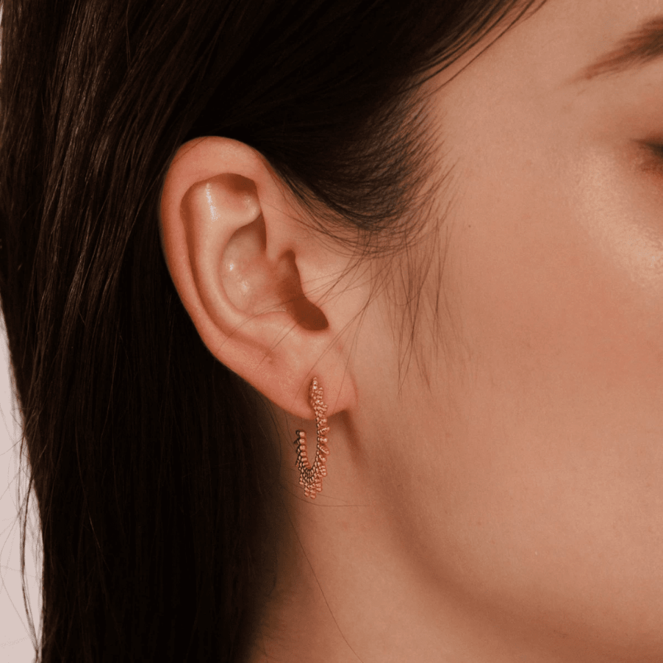 Model wearing gold Solaris earrings with sunlight reflecting off sunburst texture near collarbone