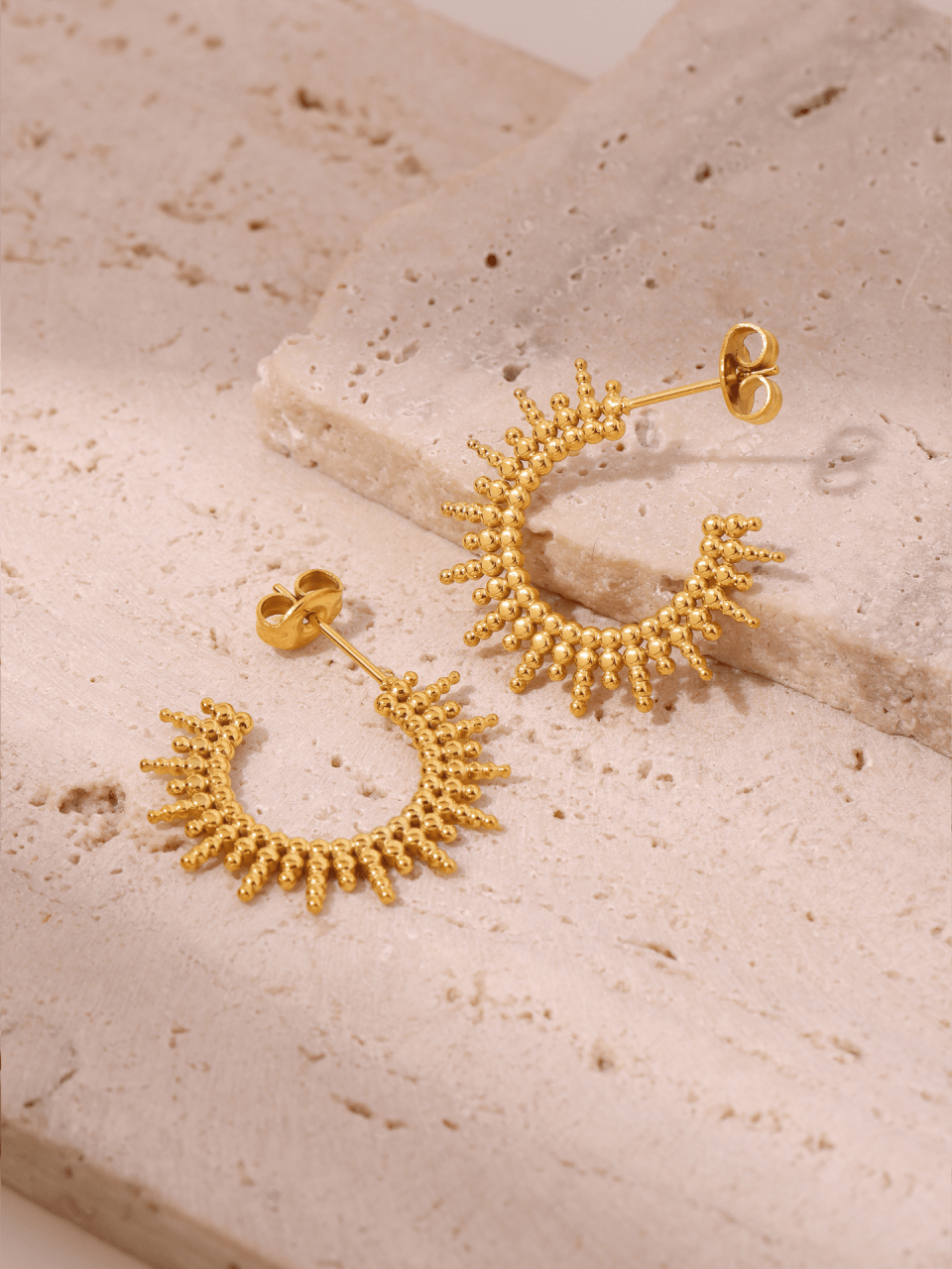 Gold and steel C-shaped hoop earrings with sunburst texture under studio lighting, 18K PVD coating reflecting light rays