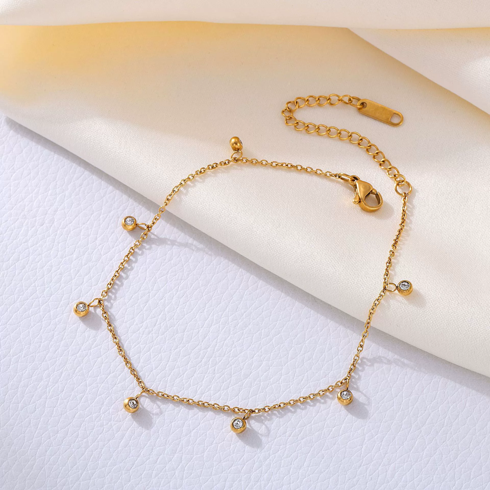 Close-up of gold permanent anklet showing CZ bead setting and seamless weld joint