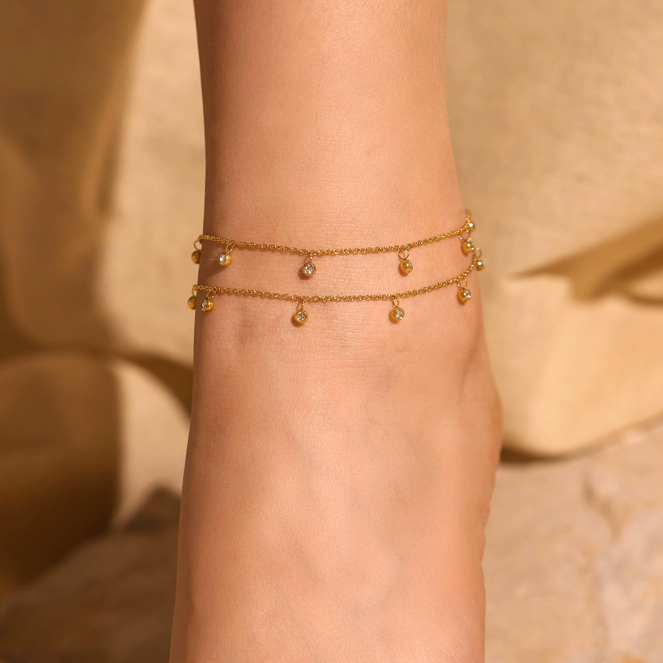 Close-up of gold permanent anklet showing CZ bead setting and seamless weld joint
