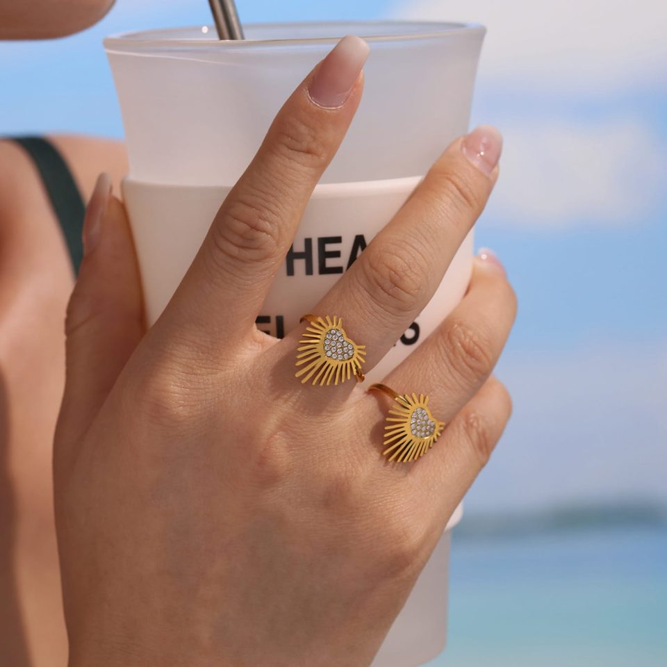 A model wearing a gold Winged Heart Open Ring with Sparkling Cubic Zirconia on her finger, holding milk tea in a casual setting.