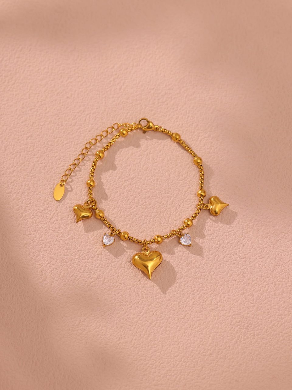 E596 Gold Heart Pendant Bracelet 17+5cm displayed in a warm-toned scene.