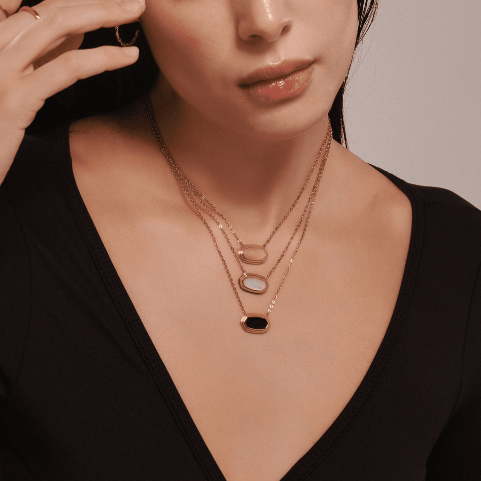 Female model wearing Oudada geometric pendant necklaces in black onyx, rose quartz, and crystal, styled with blazer for light luxury office look