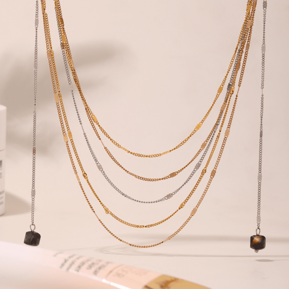 Flat lay of Oudada gold-tone layered necklace with black onyx fringe on marble, minimalist jewelry styling example