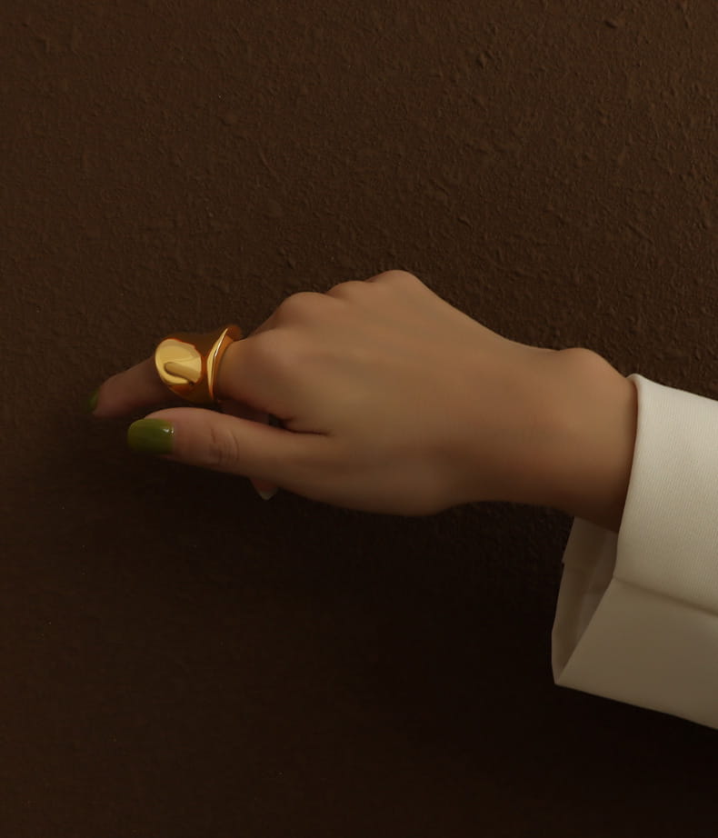 Woman wearing a gold curved statement ring with hand resting on a vintage table, styled with a white blazer