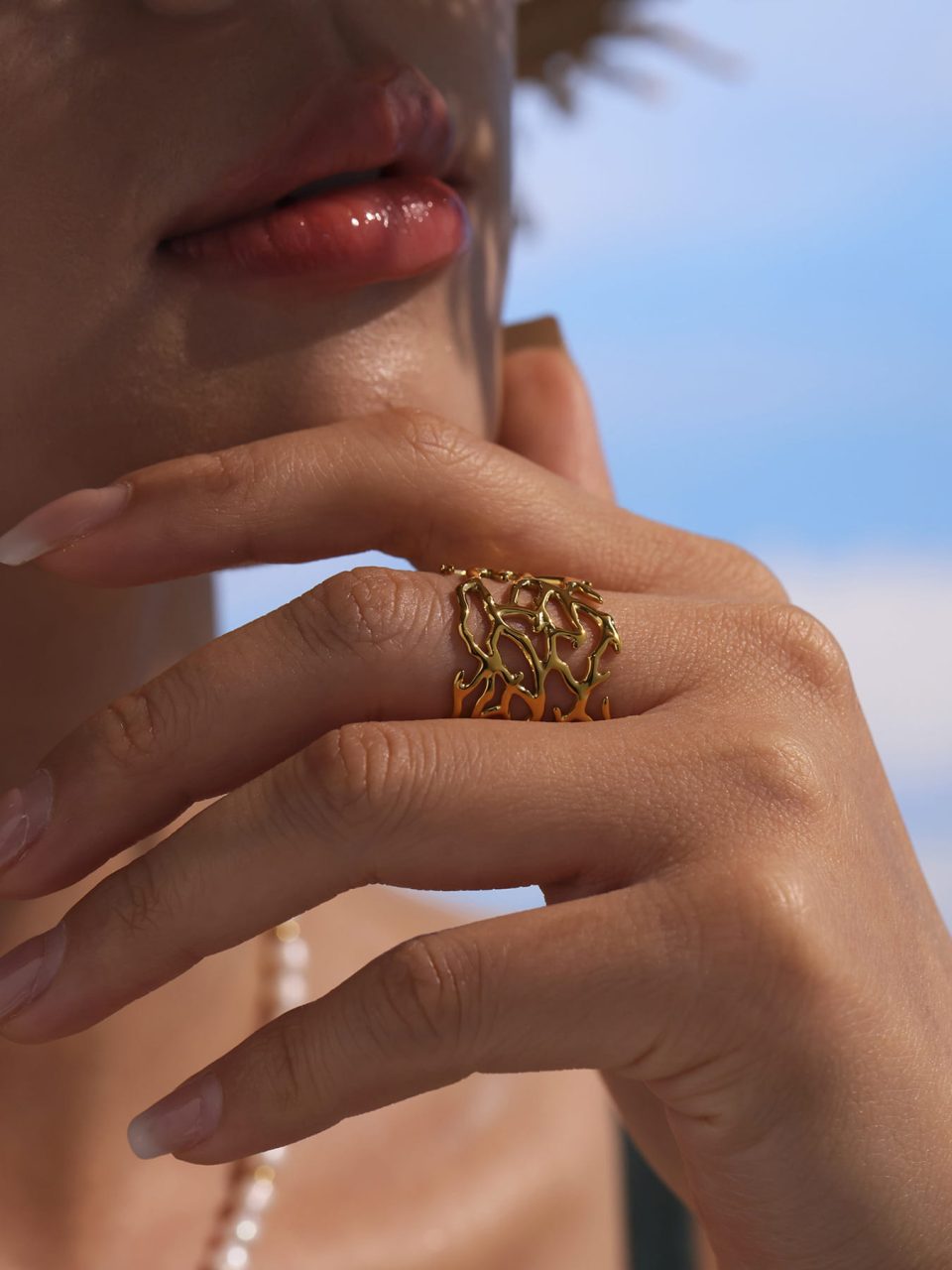 Close-up of model’s hand with gold open ring resting on chin, emphasizing textured band details