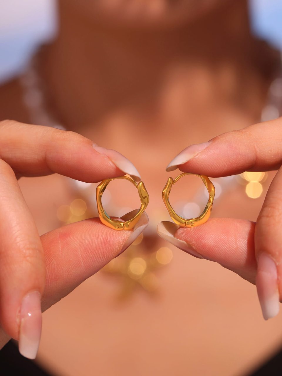 Delicate hand holding F227 gold plated hoop earring against sunlight to showcase metallic luster