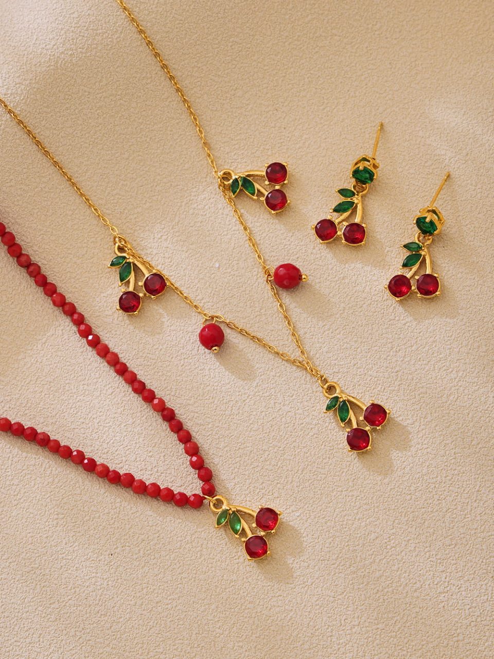 Flat lay of Oumaika’s cherry delight jewelry set with beaded necklace and glass stone earrings on pastel background