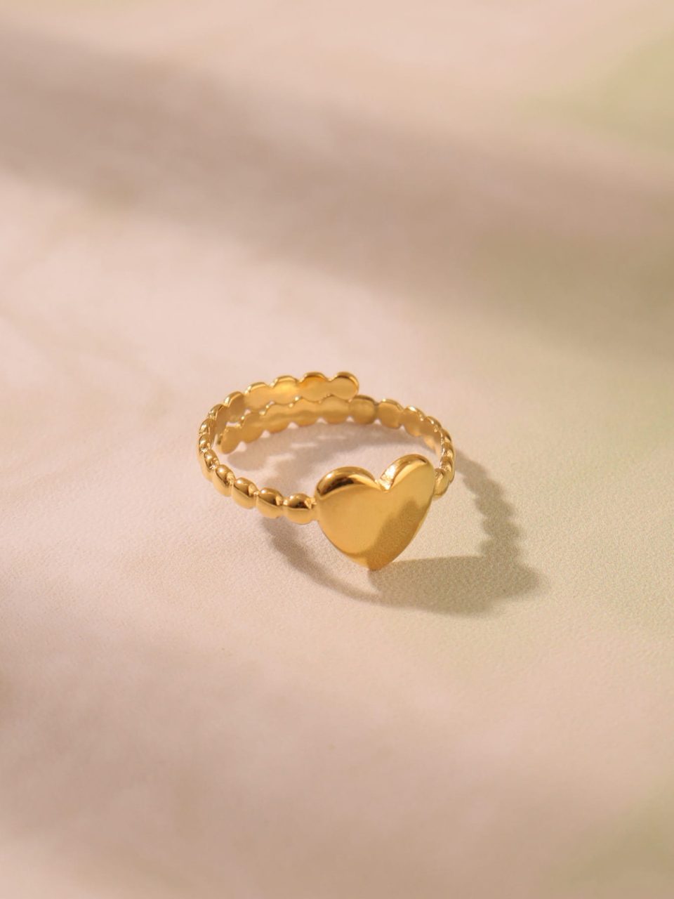 Delicate gold open heart ring on sandy beach, hypoallergenic stainless steel jewelry for everyday wear