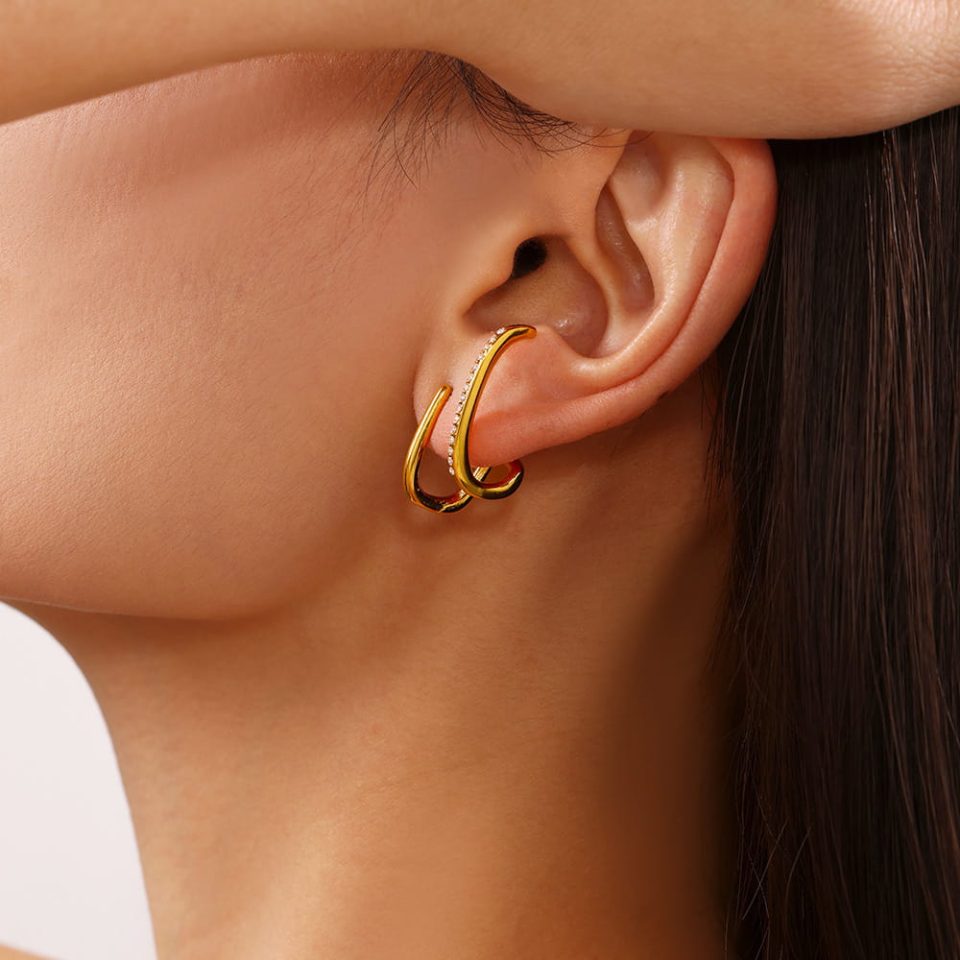 Model wearing gold-tone cubic zirconia stud earrings with a sculptural design