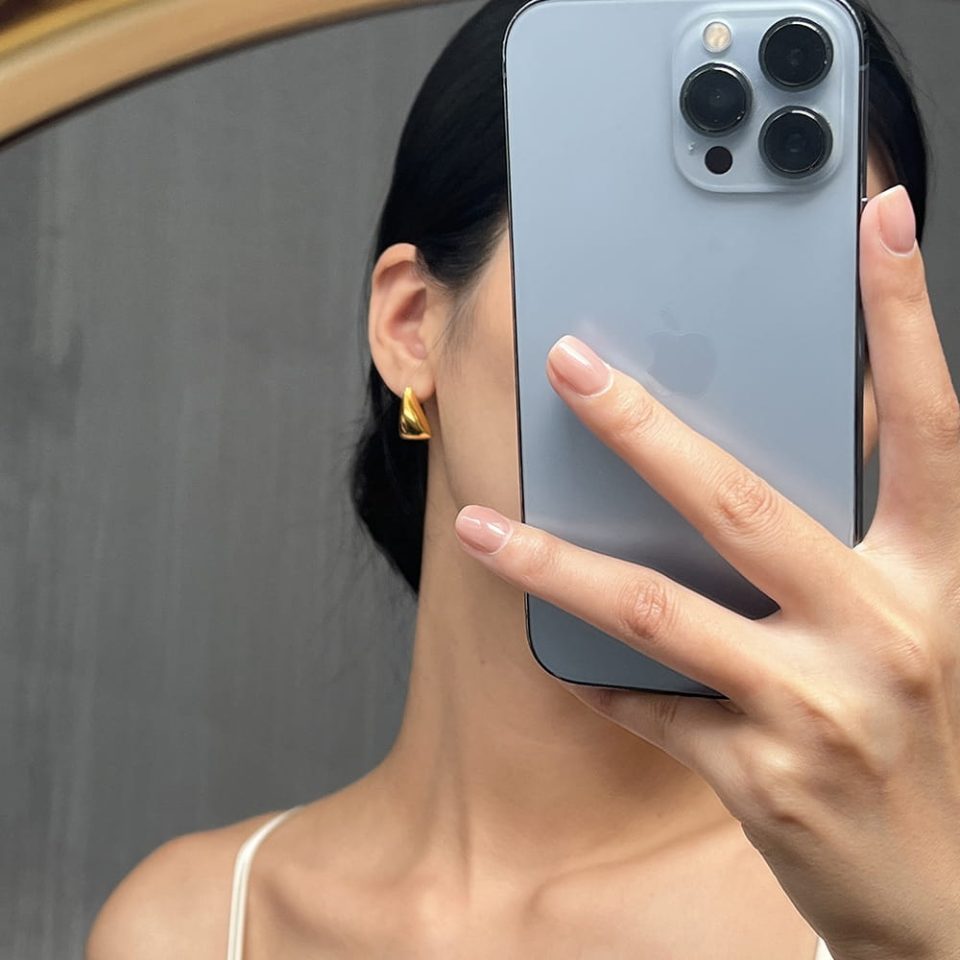 Woman wearing gold triangle stud earrings while holding an iPhone