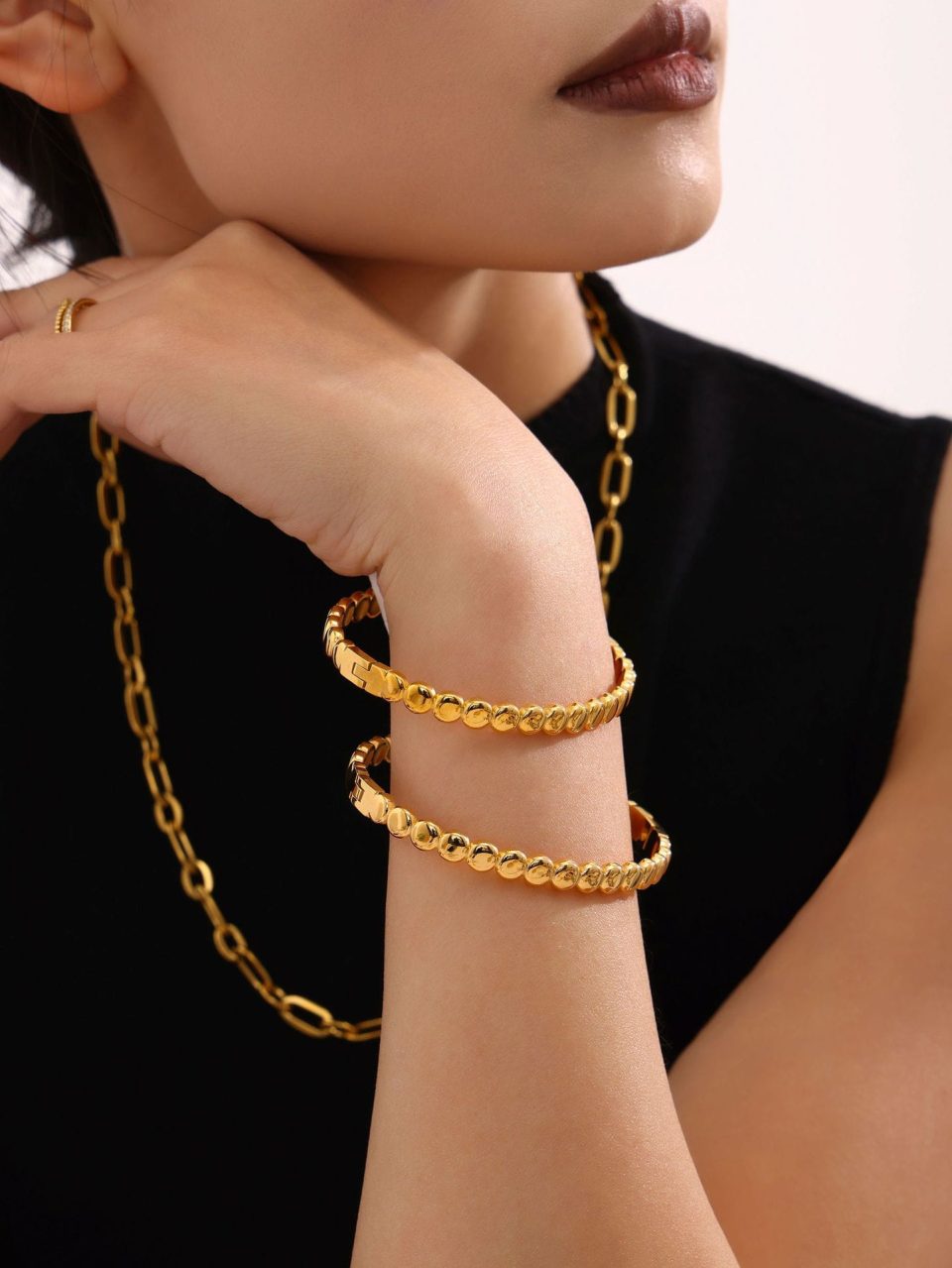 Model showcasing stackable 18K gold stainless steel bangles with bead clasps