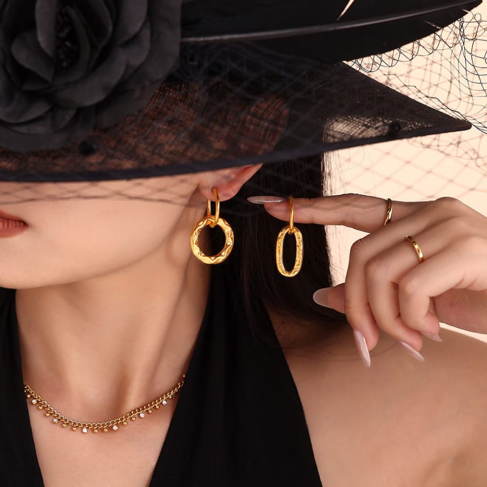 Close-up of a model holding one gold dangler earring beside another worn on ear