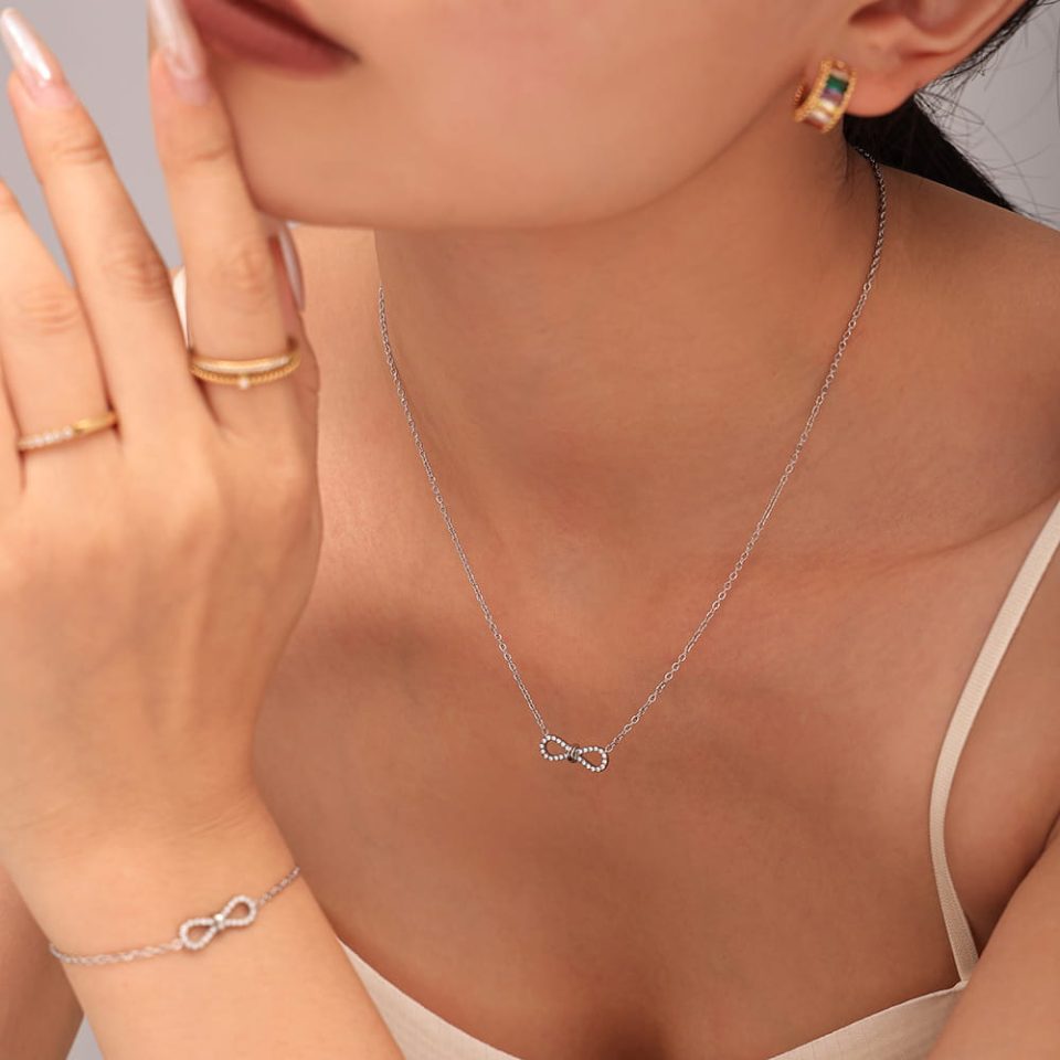 Woman wearing silver stainless steel infinity necklace with CZ on bow