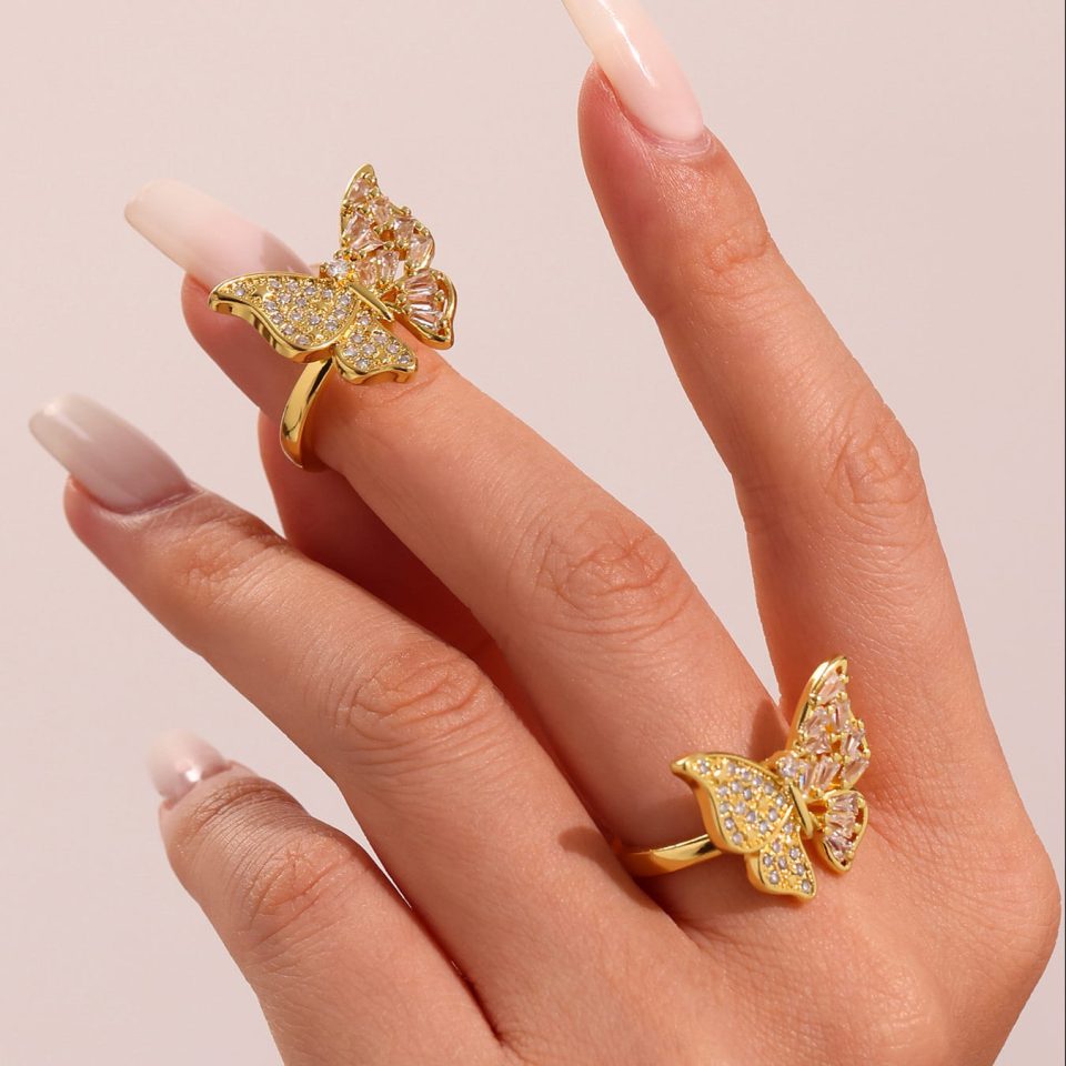 Model wearing multiple stacked rings including the Butterfly CZ Open Ring in 18K gold-plated stainless steel.