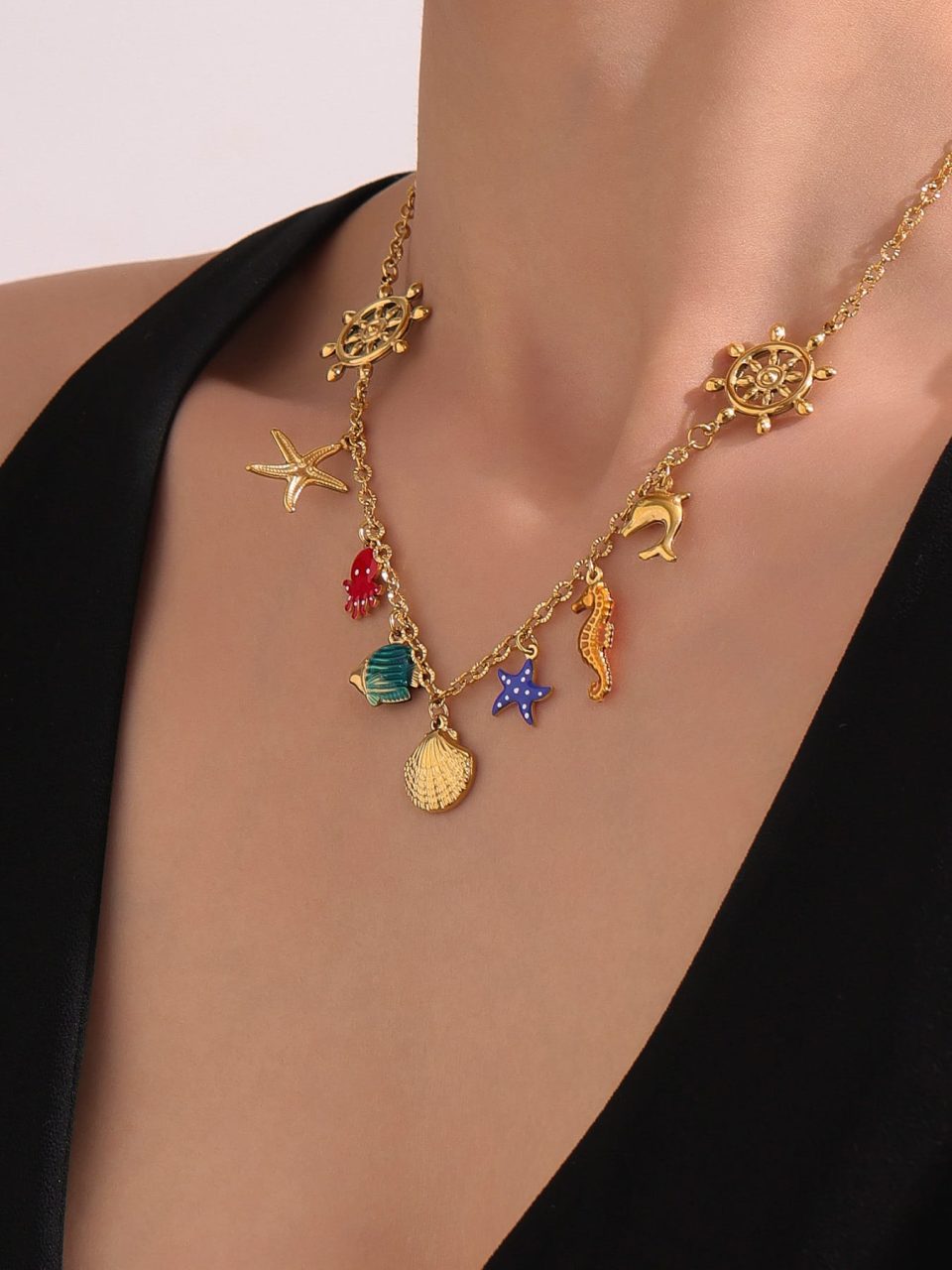 Model’s hand wearing gold ocean-themed enamel necklace with starfish and shell charms