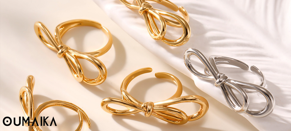Oumaika gold and silver bow rings on fabric background, Fall 2025 jewelry