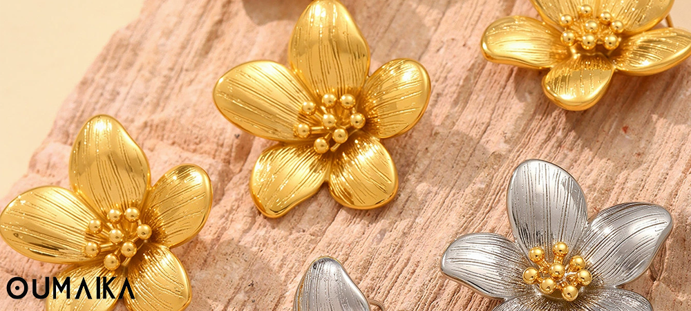 Gold and silver floral jewelry pieces from Oumaika Fall 2025 collection on textured stone surface