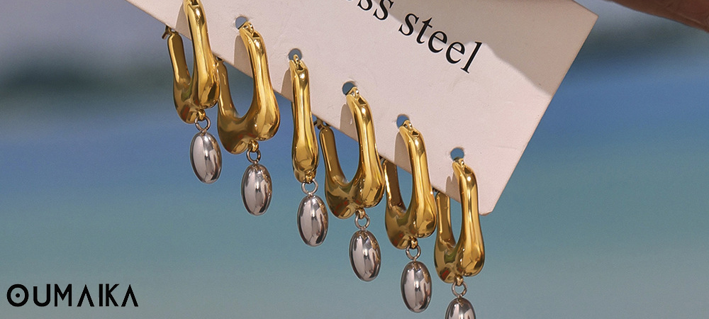 Gold and silver drop earrings displayed on "stainless steel" card, Oumaika Fall 2025