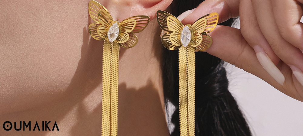 Gold butterfly drop earrings with crystal center from Oumaika, handheld close-up